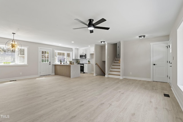 unfurnished living room with stairway, light wood-style flooring, baseboards, and visible vents