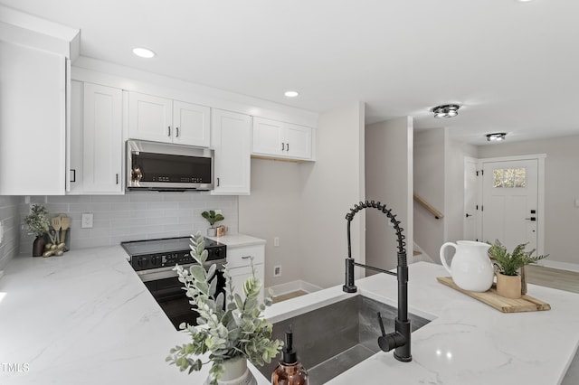 kitchen featuring stainless steel microwave, light stone counters, decorative backsplash, range with electric stovetop, and white cabinets