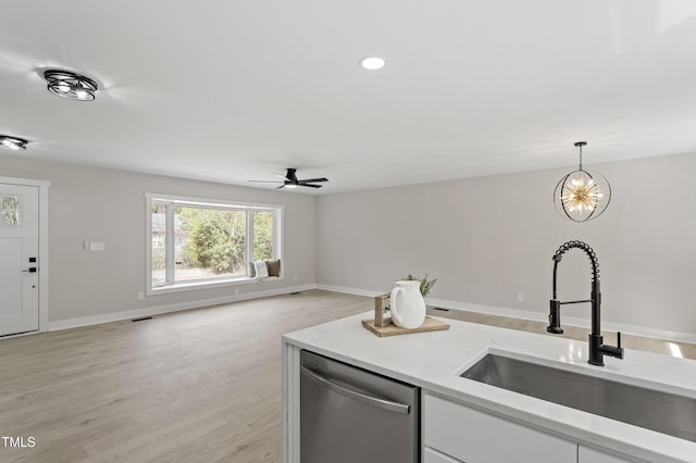 kitchen featuring decorative light fixtures, dishwasher, light wood-style floors, white cabinetry, and a sink