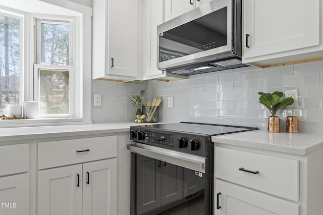 kitchen with electric stove, light stone counters, stainless steel microwave, white cabinets, and decorative backsplash