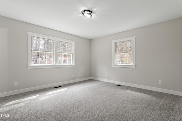 carpeted empty room with a healthy amount of sunlight, visible vents, and baseboards