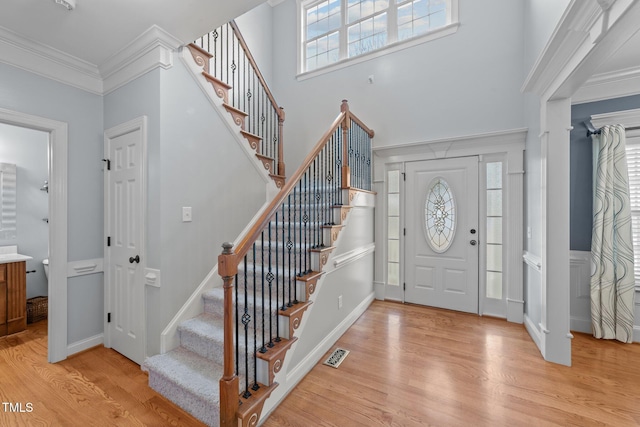 foyer entrance featuring light wood-style flooring, a high ceiling, visible vents, ornamental molding, and stairway