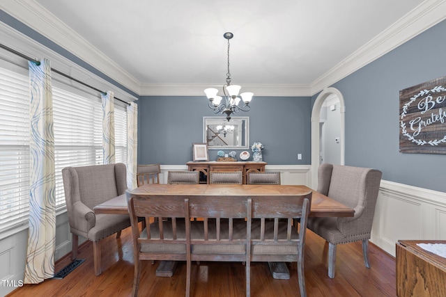 dining room with arched walkways, wainscoting, an inviting chandelier, and wood finished floors