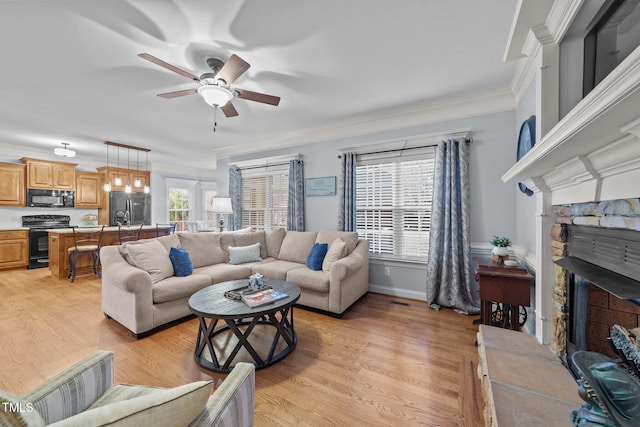 living room with crown molding, a fireplace, light wood-style flooring, and a ceiling fan