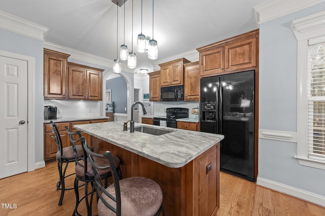 kitchen featuring arched walkways, brown cabinetry, light wood-style floors, a sink, and black appliances