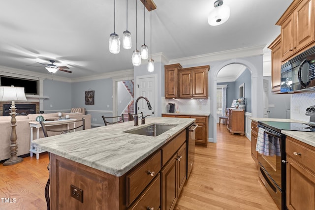 kitchen featuring arched walkways, a sink, light wood-type flooring, black appliances, and a glass covered fireplace