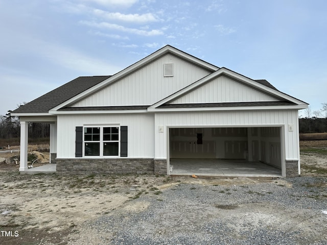 view of front facade featuring gravel driveway, a garage, stone siding, and a shingled roof