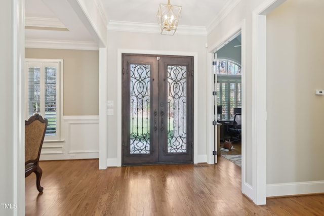 foyer entrance with a chandelier, ornamental molding, french doors, and wood finished floors