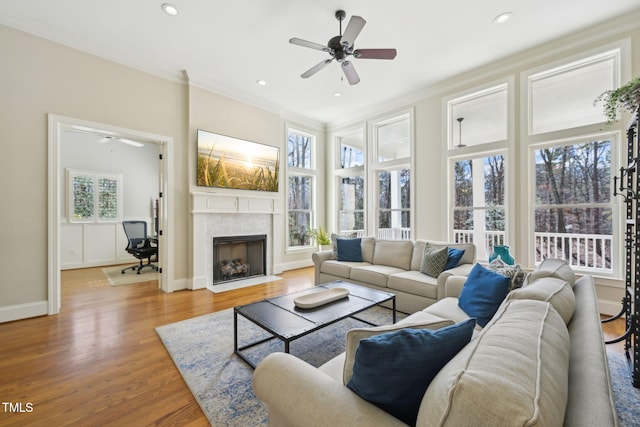 living room with light wood-type flooring, a fireplace with flush hearth, ornamental molding, baseboards, and ceiling fan