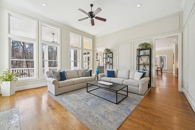 living area with a decorative wall, visible vents, wood finished floors, and ornamental molding