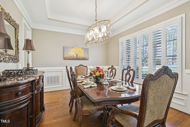 dining room with visible vents, ornamental molding, wainscoting, light wood-style floors, and a raised ceiling