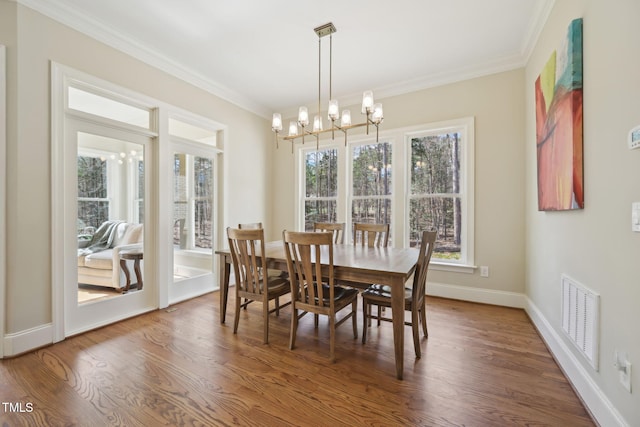 dining room featuring a chandelier, visible vents, crown molding, and wood finished floors