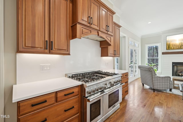 kitchen featuring brown cabinetry, range with two ovens, light countertops, crown molding, and a large fireplace