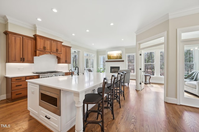 kitchen featuring light countertops, brown cabinets, appliances with stainless steel finishes, a fireplace, and wood finished floors