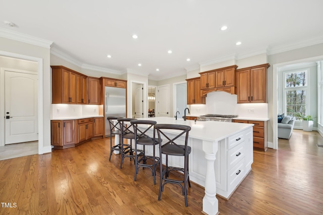 kitchen featuring a breakfast bar area, brown cabinetry, an island with sink, stainless steel appliances, and light wood-type flooring