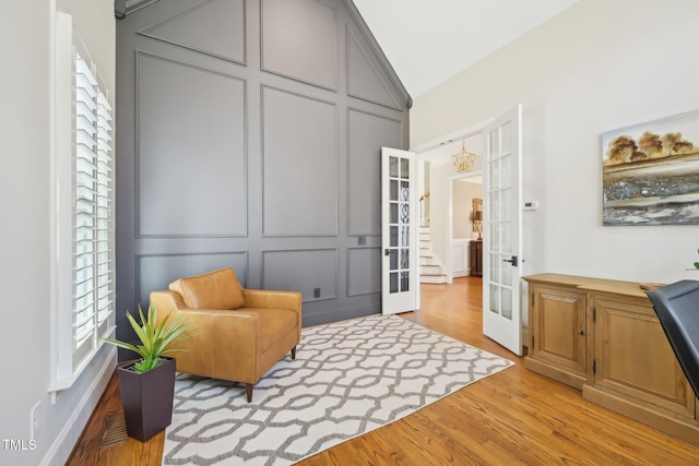 living area featuring a decorative wall, french doors, light wood-style floors, and vaulted ceiling