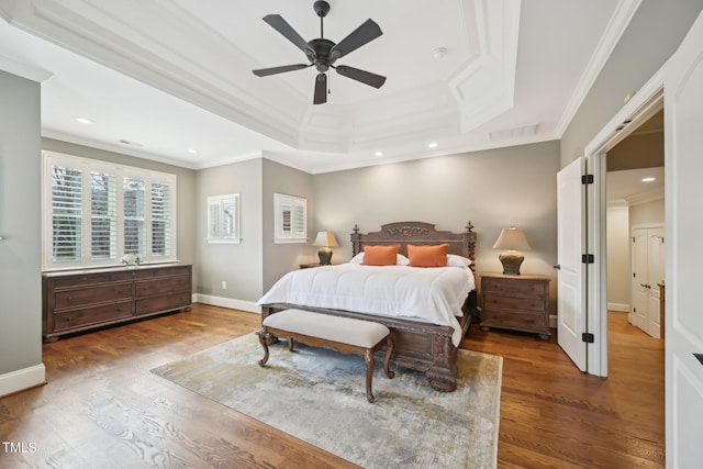 bedroom with baseboards, crown molding, a tray ceiling, and wood finished floors