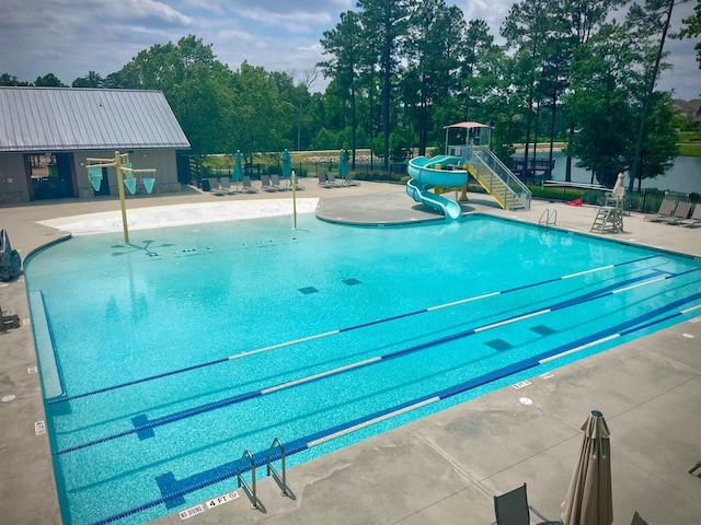 community pool featuring a patio area, fence, a water slide, and playground community