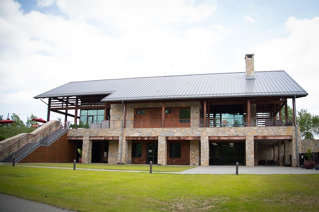 back of house with a standing seam roof, a lawn, metal roof, stone siding, and a chimney