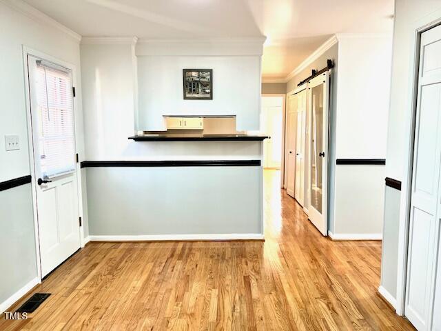 interior space with a barn door, light wood-type flooring, visible vents, and crown molding