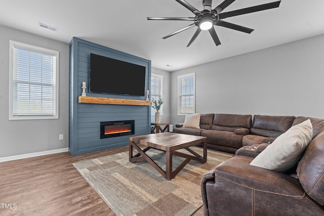 living area featuring a fireplace, wood finished floors, a ceiling fan, visible vents, and baseboards