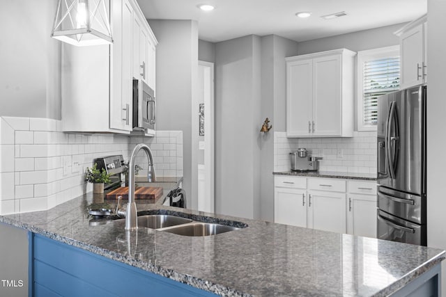 kitchen with dark stone counters, appliances with stainless steel finishes, a sink, and white cabinetry