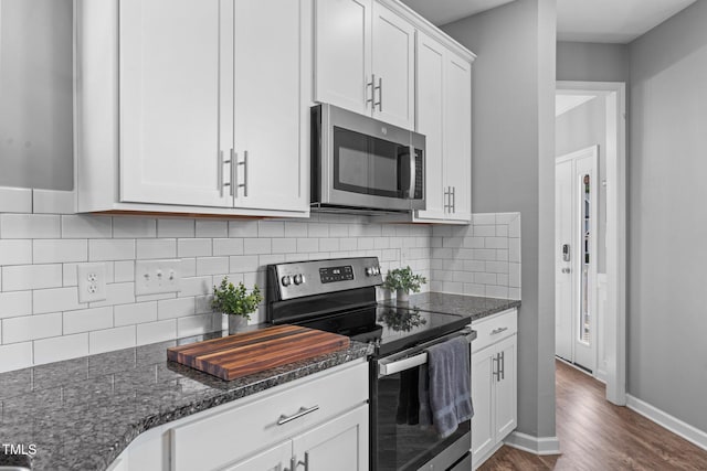 kitchen with tasteful backsplash, dark stone counters, dark wood-style floors, stainless steel appliances, and white cabinetry