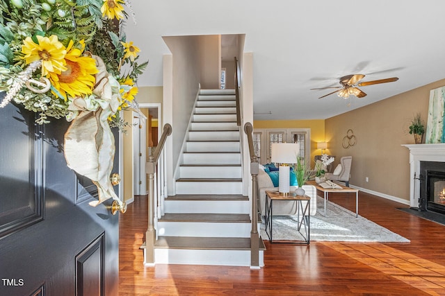 stairs featuring a fireplace with flush hearth, wood finished floors, baseboards, and ceiling fan