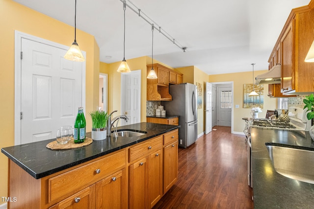 kitchen featuring backsplash, under cabinet range hood, brown cabinets, stainless steel appliances, and a sink