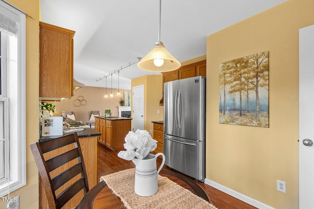 kitchen featuring decorative light fixtures, freestanding refrigerator, rail lighting, brown cabinetry, and dark wood-style flooring