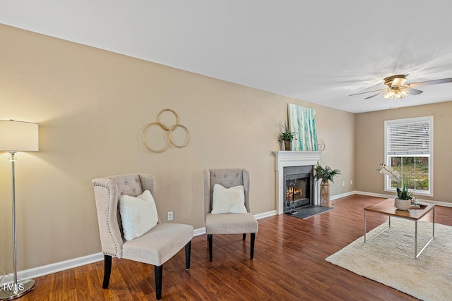 sitting room with ceiling fan, baseboards, a fireplace with flush hearth, and wood finished floors