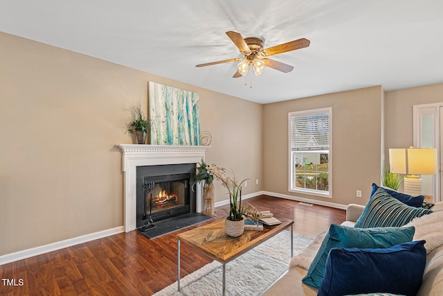 living area with a fireplace with flush hearth, wood finished floors, baseboards, and ceiling fan