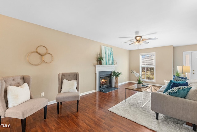 living room featuring a fireplace with flush hearth, a ceiling fan, baseboards, and wood finished floors