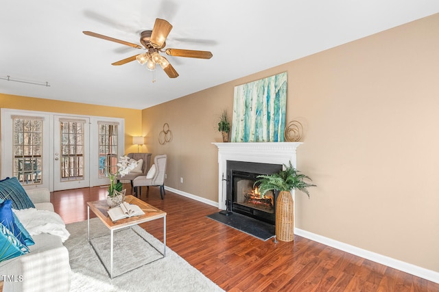 living room with a ceiling fan, a fireplace with flush hearth, wood finished floors, and baseboards