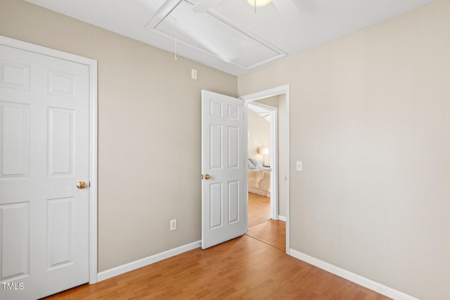 unfurnished bedroom featuring attic access, baseboards, light wood-type flooring, and ceiling fan