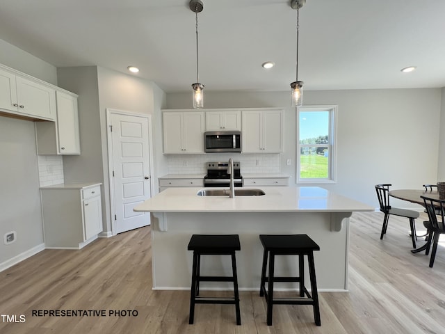 kitchen with stainless steel appliances, a sink, white cabinetry, light countertops, and light wood finished floors