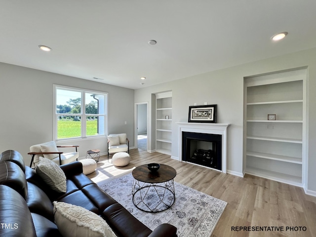 living area with built in shelves, baseboards, light wood-style floors, a fireplace, and recessed lighting