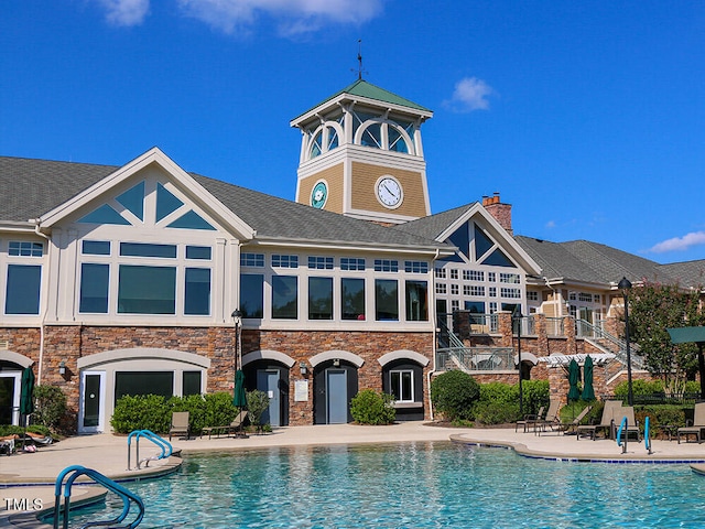 exterior space featuring a patio, a community pool, roof with shingles, and a chimney