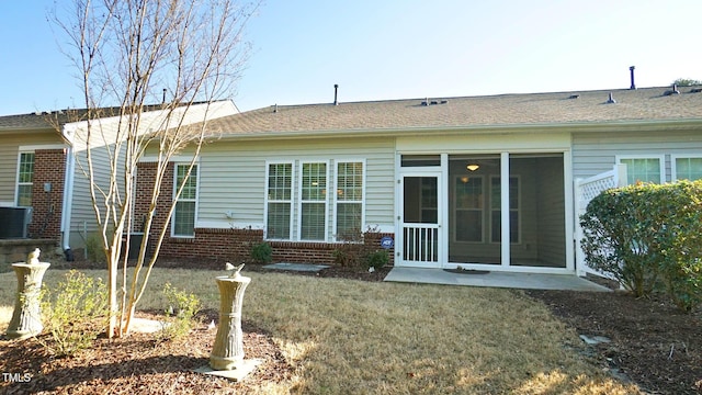 rear view of house with a lawn, brick siding, a sunroom, and roof with shingles