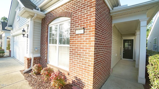 entrance to property with concrete driveway, an attached garage, brick siding, and roof with shingles