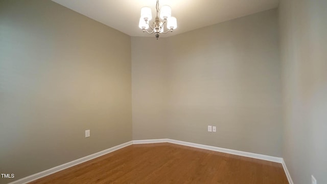 empty room featuring a notable chandelier, baseboards, and wood finished floors