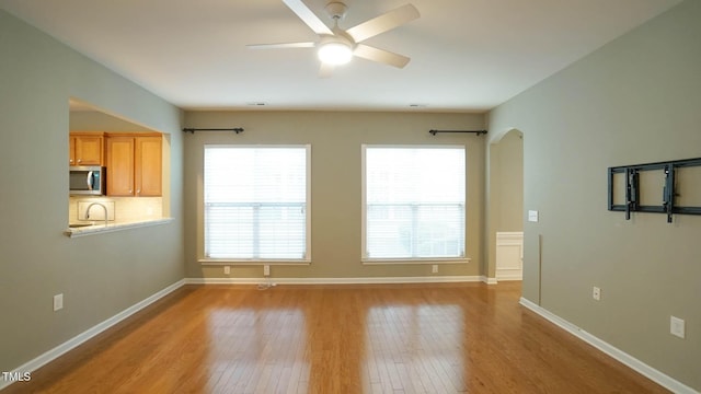 interior space featuring ceiling fan, baseboards, arched walkways, and wood finished floors