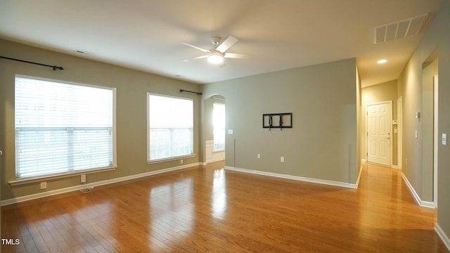 empty room featuring visible vents, arched walkways, baseboards, and wood finished floors