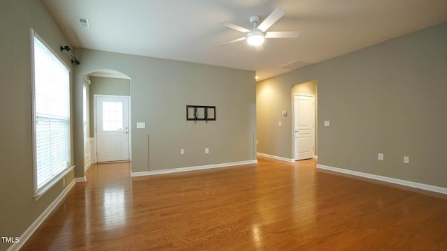 empty room with visible vents, ceiling fan, baseboards, light wood-style floors, and arched walkways