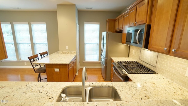 kitchen featuring brown cabinetry, light stone countertops, stainless steel appliances, and a sink