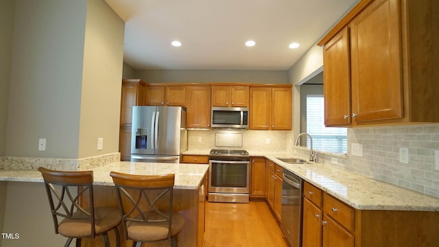 kitchen featuring a peninsula, a sink, stainless steel appliances, a kitchen breakfast bar, and brown cabinets