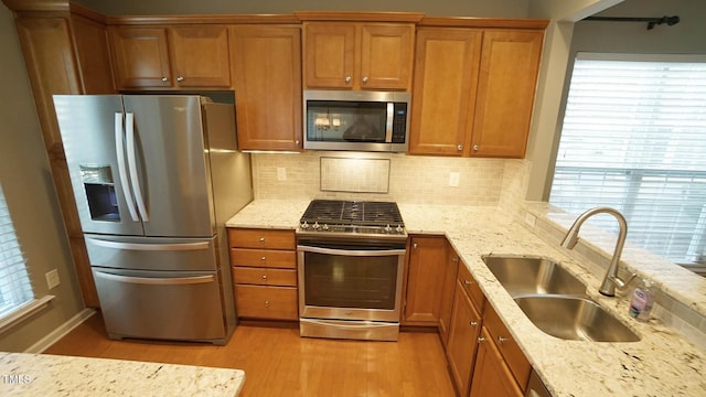 kitchen with brown cabinets, stainless steel appliances, light wood-type flooring, and a sink