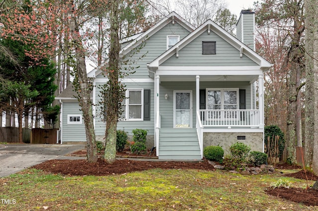 view of front of home with driveway, covered porch, a chimney, and fence