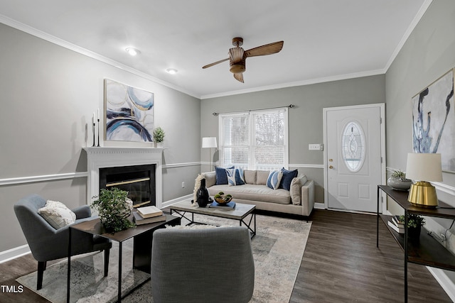 living room featuring dark wood-type flooring, a glass covered fireplace, crown molding, and baseboards