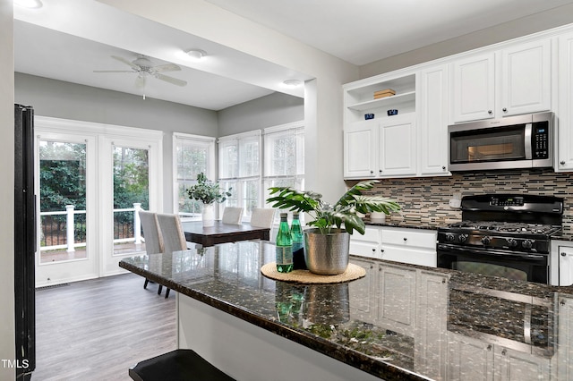 kitchen with stainless steel microwave, decorative backsplash, gas stove, white cabinetry, and dark stone counters